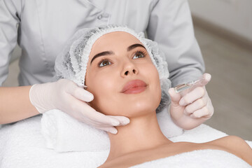 Professional cosmetologist holding skincare ampoule while working with client in clinic, closeup