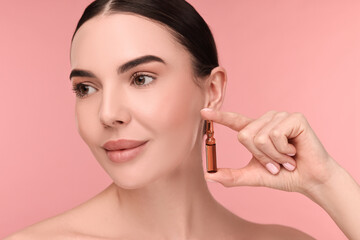 Beautiful young woman holding skincare ampoule on pink background