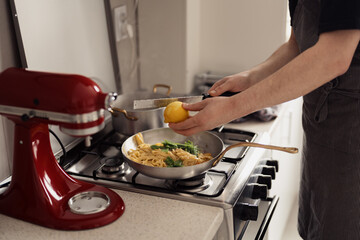 Close-up of hands zesting lemon on pasta in a home kitchen setting.