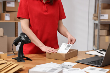 Parcel packing. Post office worker sticking barcode on box at wooden table indoors, closeup