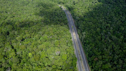 Aerial view of a deserted road cutting through a dense forest, symbolizing concepts of travel,...