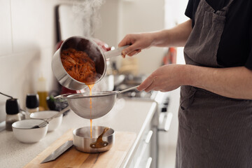 Person in apron strains steaming shrimps over pot in kitchen