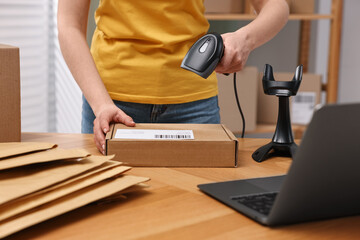 Parcel packing. Post office worker with scanner reading barcode at wooden table indoors, closeup