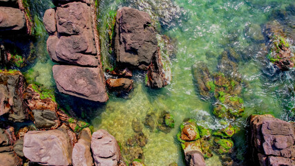 Aerial view of a rugged coastline with red rock formations and lush greenery meeting the turquoise...