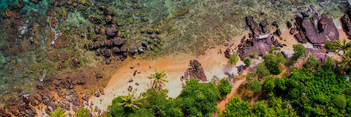 Aerial view of a rugged coastline with red rock formations and lush greenery meeting the turquoise...