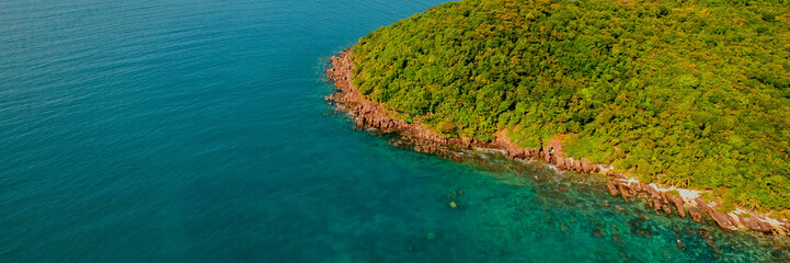 Aerial view of a rugged coastline with red rock formations and lush greenery meeting the turquoise sea, suitable for Earth Day and nature conservation topics