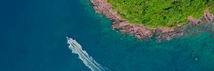 Aerial view of a speedboat cruising along the coast with lush greenery and rocky shoreline, ideal...