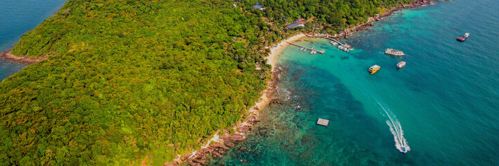 Aerial view of a rugged coastline with red rock formations and lush greenery meeting the turquoise...