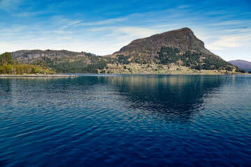 Island with rocks and trees in the fjord in front of the open sea in Norway.