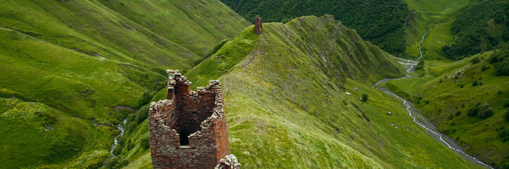 Panoramic view of misty green mountains with an ancient solitary tower, ideal for articles on...
