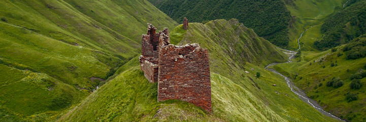Ancient stone fortress ruins atop a grassy ridge in a lush green valley, symbolizing historical...