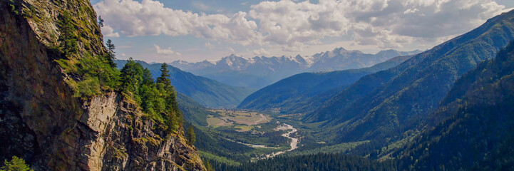 Naklejka premium Breathtaking view of a verdant alpine valley and towering mountains under a clear sky, ideal for Earth Day and environmental conservation themes