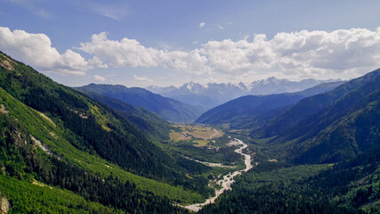 Breathtaking view of a verdant alpine valley and towering mountains under a clear sky, ideal for...