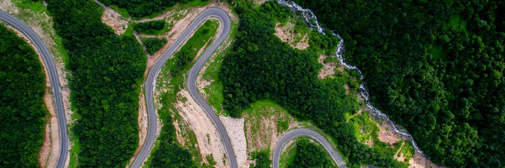 Aerial view of a winding road snaking through a lush green forest, conceptually ideal for travel, adventure, and environmental themes