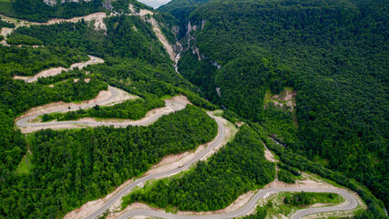 Aerial view of a winding road snaking through a lush green forest, conceptually ideal for travel,...
