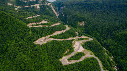Aerial view of a winding road snaking through a lush green forest, conceptually ideal for travel,...