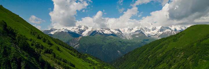 Fototapeta premium Lush green mountain slopes lead to snow-capped peaks under a clear sky, ideal for Earth Day and International Mountain Day themes