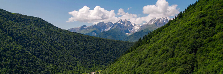 Lush green mountain slopes lead to snow-capped peaks under a clear sky, ideal for Earth Day and International Mountain Day themes