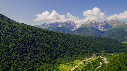 Lush green mountain slopes lead to snow-capped peaks under a clear sky, ideal for Earth Day and...