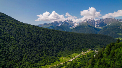 Lush green mountain slopes lead to snow-capped peaks under a clear sky, ideal for Earth Day and...