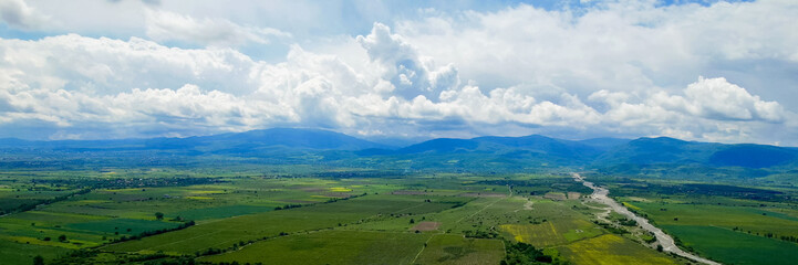 Panoramic view of a serene valley with a meandering river, green fields, and distant mountains under a cloudy sky, suitable for Earth Day and World Environment Day concepts