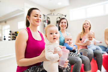 Baby movement class. Parents helping babies to improve motor skills, proper movement on fitball. Pediatric physical therapist leading class. Mothers exercising with babies.