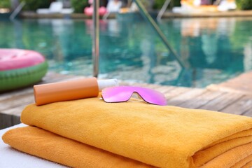 Beach towels, sunglasses and sunscreen on sun lounger near outdoor swimming pool, closeup. Luxury...