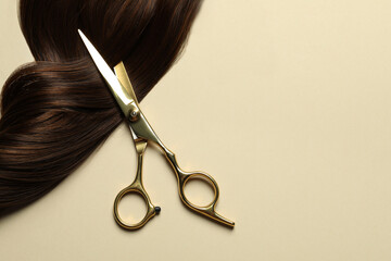 Professional scissors with brown hair strand on beige background, top view. Space for text