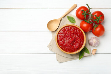 Homemade tomato sauce in bowl, spoon and fresh ingredients on white wooden table, flat lay. Space for text