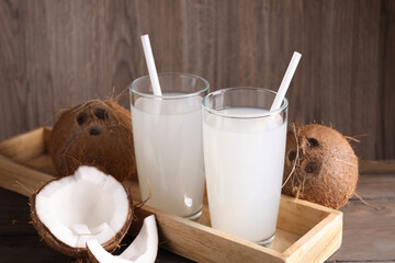 Glasses of coconut water with straws and nuts on wooden table