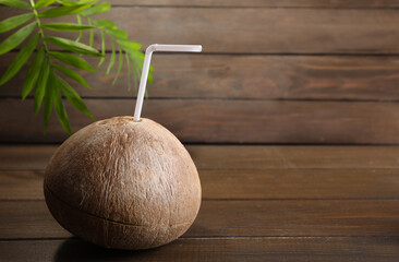 Coconut water. Fresh nut with straw on wooden table, space for text
