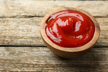 Tasty ketchup in bowl on wooden table, space for text. Tomato sauce