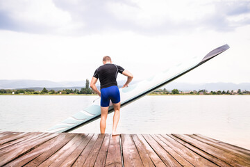 Young canoeist putting canoe into water, standing on wooden dock. Concept of canoeing as dynamic...