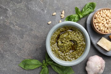 Tasty pesto sauce in bowl, basil, pine nuts, cheese and garlic on grey table, flat lay. Space for...