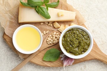 Tasty pesto sauce in bowl, basil, pine nuts, garlic, oil and cheese on light grey table, top view