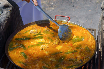 close-up of the hand of a cook cooking a typical Spanish paella over a fire in the countryside