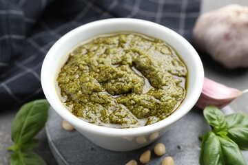 Tasty pesto sauce in bowl, basil, pine nuts and garlic on table, closeup
