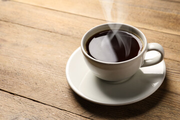 Steaming coffee in cup on wooden table. Space for text