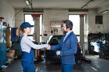 Female auto mechanic talking with customer, shaking hands. Beautiful woman working in a garage,...