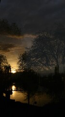 Vertical shot of a cloudy sunset sky with silhouettes of trees and a lake in Kashmir