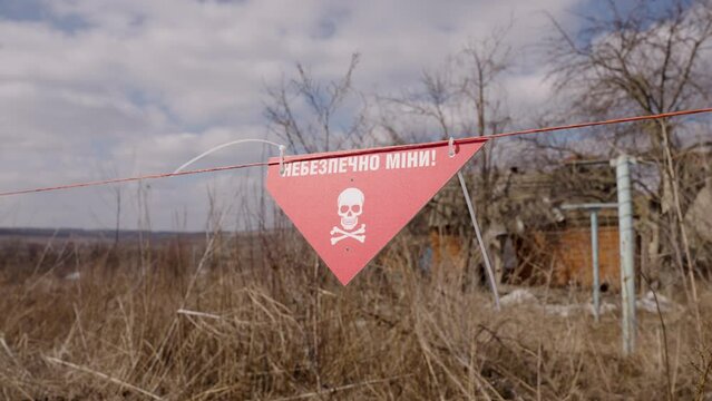 Attention mines warning sign with skull and crossbones logo hang off wire fence