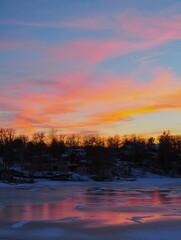 Obraz premium Scenic view of a colorful sunset over the frozen lake and silhouettes of trees