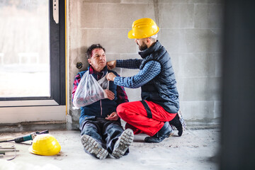 Colleague giving first aid to injured worker, in pain after accident at construction site Concept...