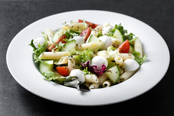 Pasta salad with vegetables and mozzarella cheese on black background 