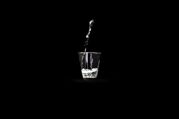 Glass with a stream of water flowing into it on a black background