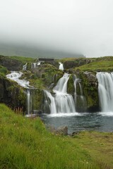Beautiful scene of Kirkjufellsfoss waterfall with green grass on a cloudy day