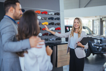 Young couple buying a car. Salesperson offering help to a couple in choosing a right color for...