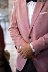 Obraz premium Vertical shot of with crossed hands wearing a pink suit during his wedding ceremony