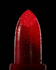 Closeup vertical shot of the red lipstick with water droplets on the black background