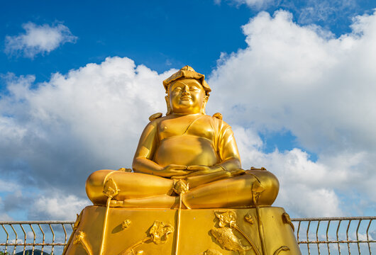 Yellow laughing smiling Buddha against tropical sky in Phuket, Thailand